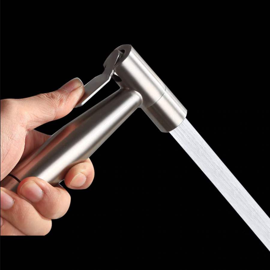 Stainless steel hand held bidet sprayer on its wall bracket beside a toilet